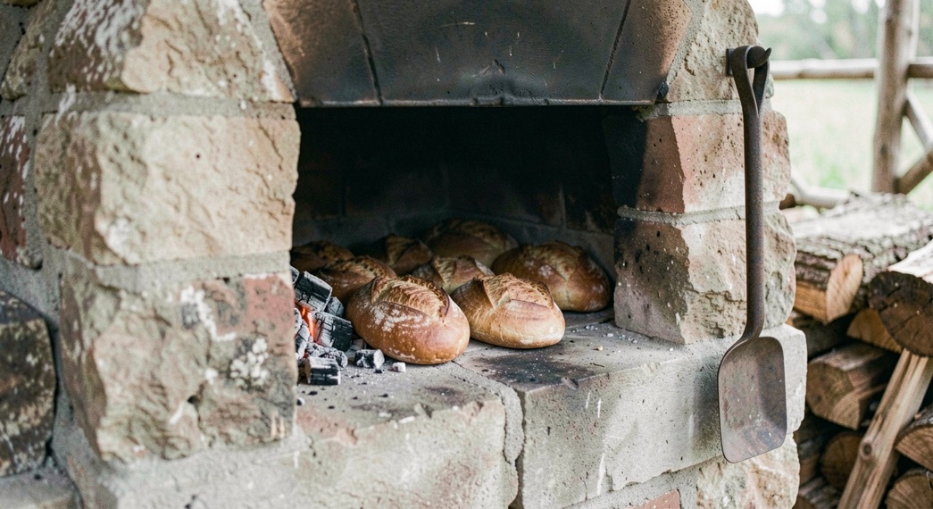 Interior de un obrador de panadería al amanecer, con una bandeja de hogazas recién salidas del horno y, en primer plano, una cesta de huevos frescos con el código impreso en la cáscara, luz cálida lateral y encuadre cerrado.